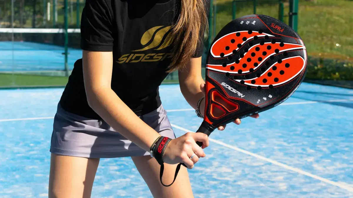 Jugadora de pádel sujetando una pala roja y negra en una pista azul