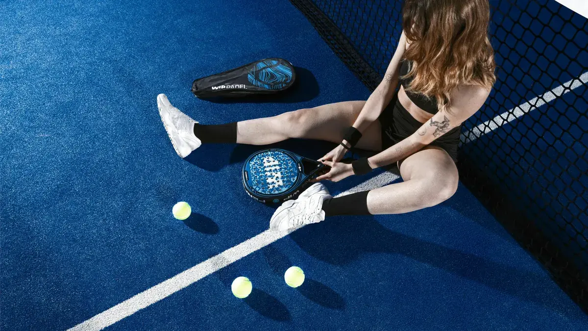 Jugadora de pádel sentada en la pista con zapatillas blancas, pala y pelotas