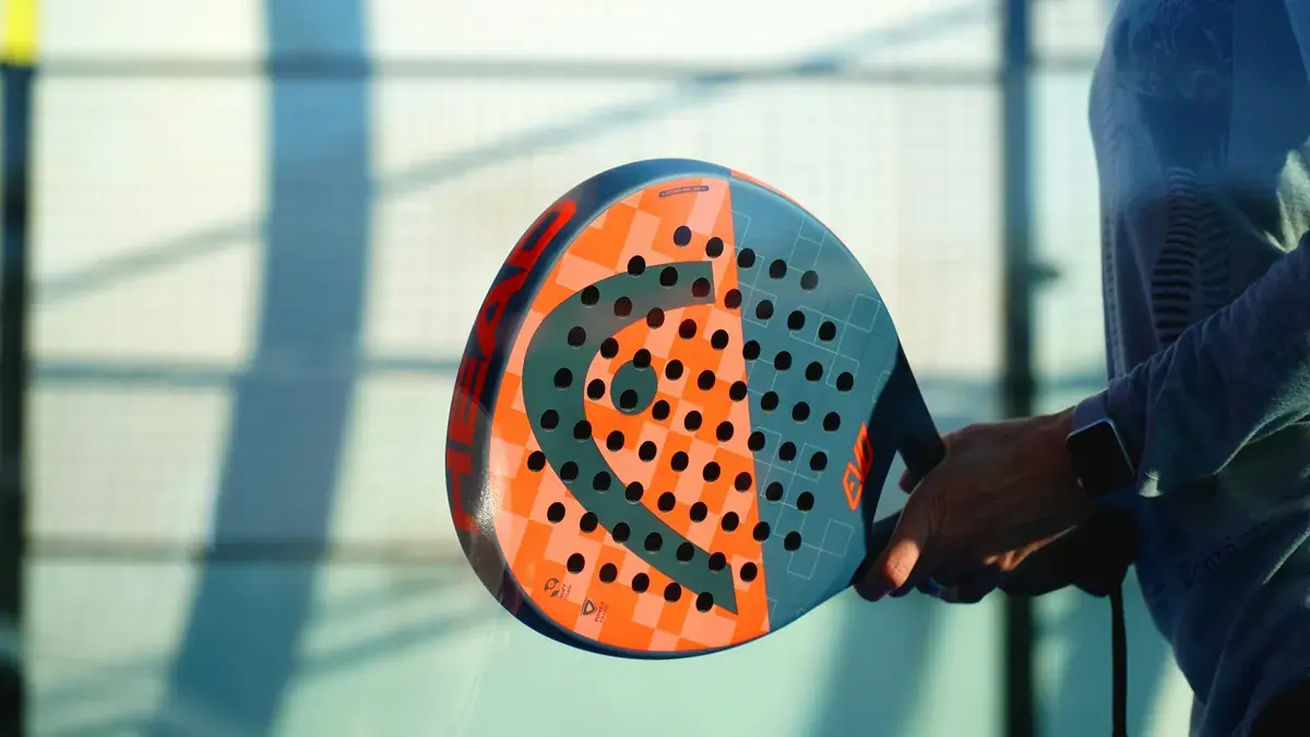 Mano sujetando una pala de pádel Head naranja con el logotipo visible